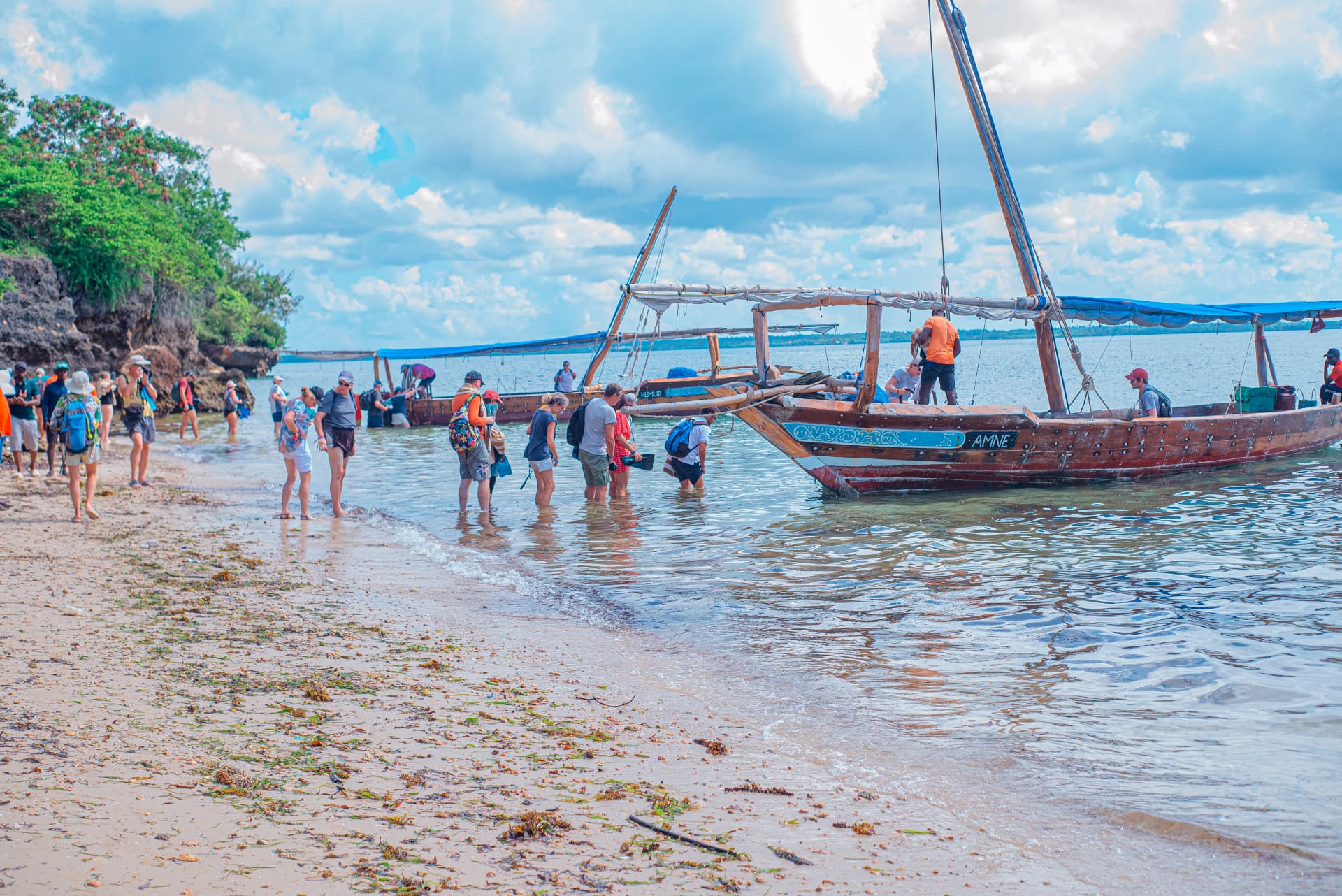 Visitors wading ashore beside traditional dhows on a sandy beach in Zanzibar